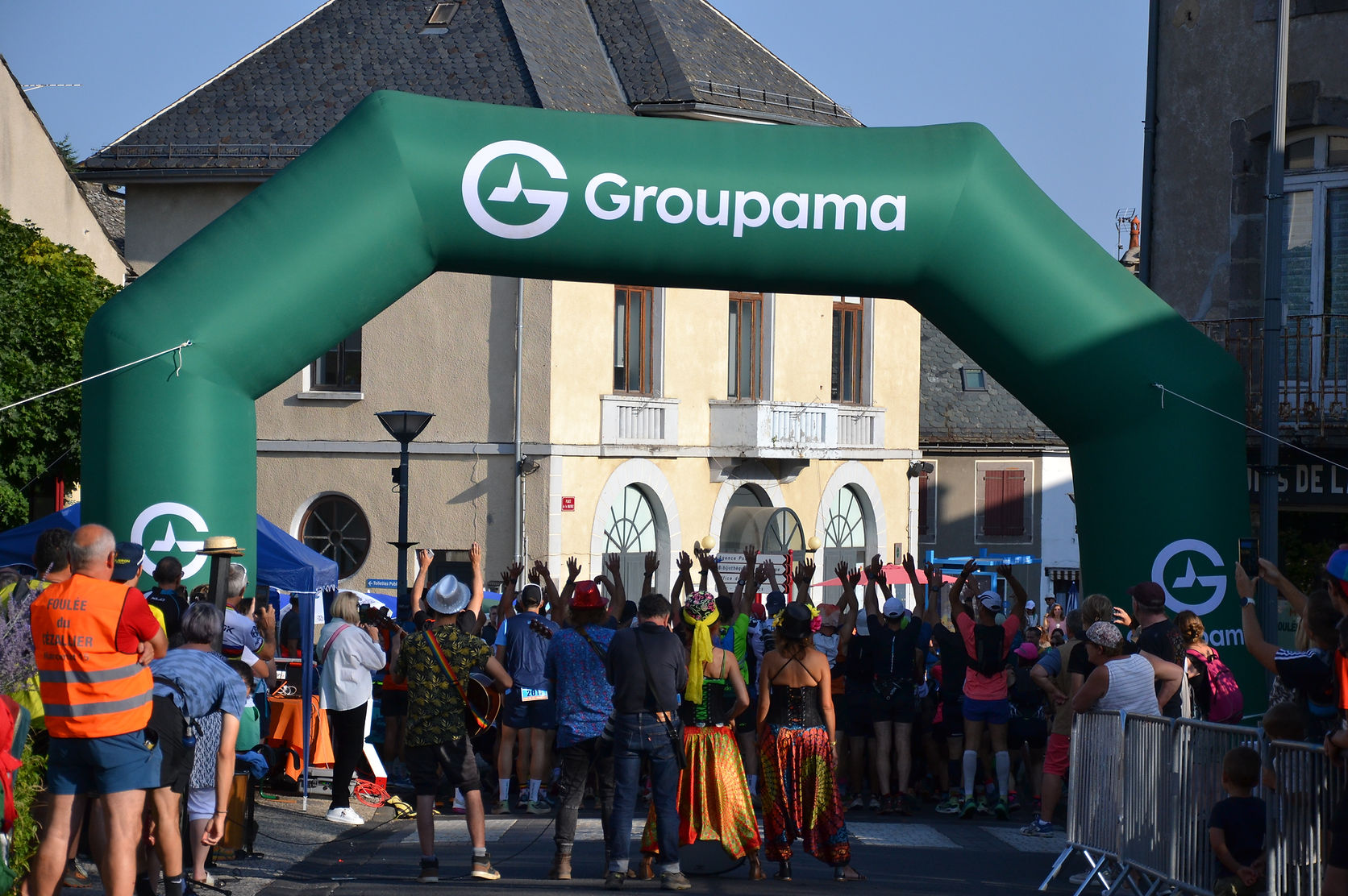 Les coureurs sous l'arche de départ Groupama, encouragés par la foule et les musiciens dans la rue de Marcenat